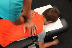 A person gently massaging their sore shoulder while seated at home, with a look of mild discomfort.